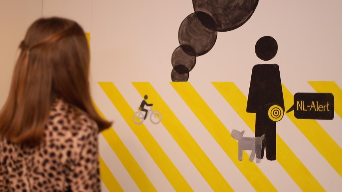 Kind staat voor muur met NL alert logo er op