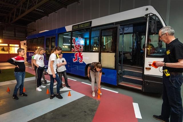 Kinderen langs een bus bezig met het uitzoeken van de dode hoek onder begeleiding