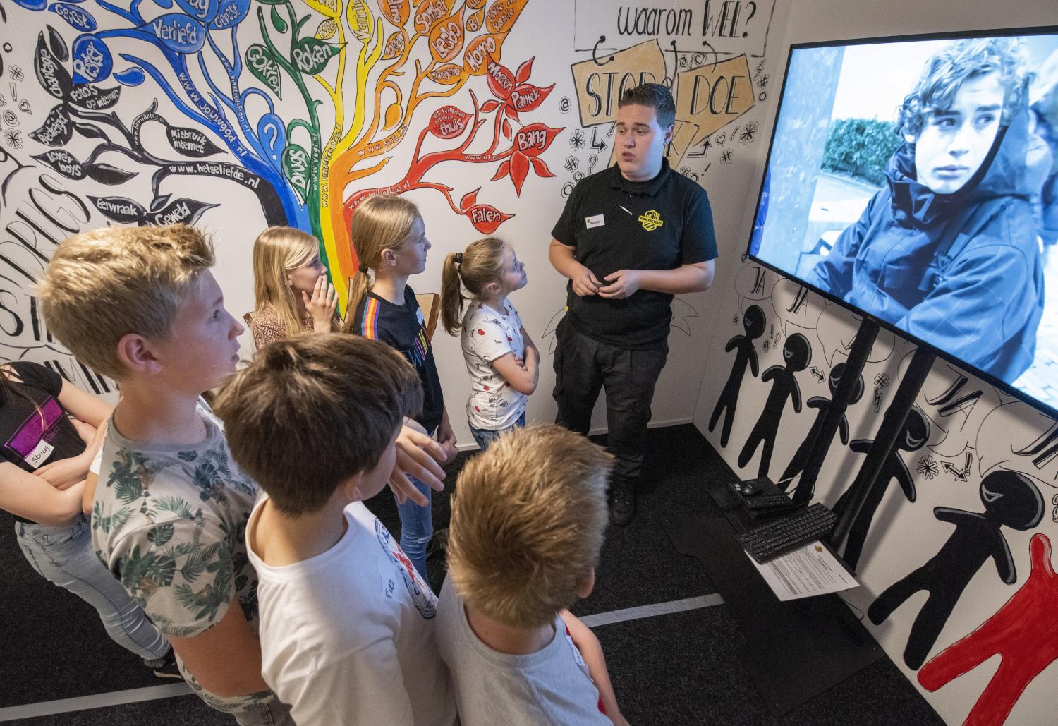 Kinderen beleven het scenario 'Groepsdruk' en kijken samen met een begeleider naar een video op groot scherm